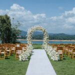 an outdoor wedding setup featuring wooden chairs and a floral archway